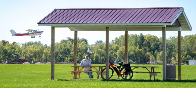 - Airlake Airport: A spectator sits under a shaded pavilion next to a bike as a small plane takes off over a field.